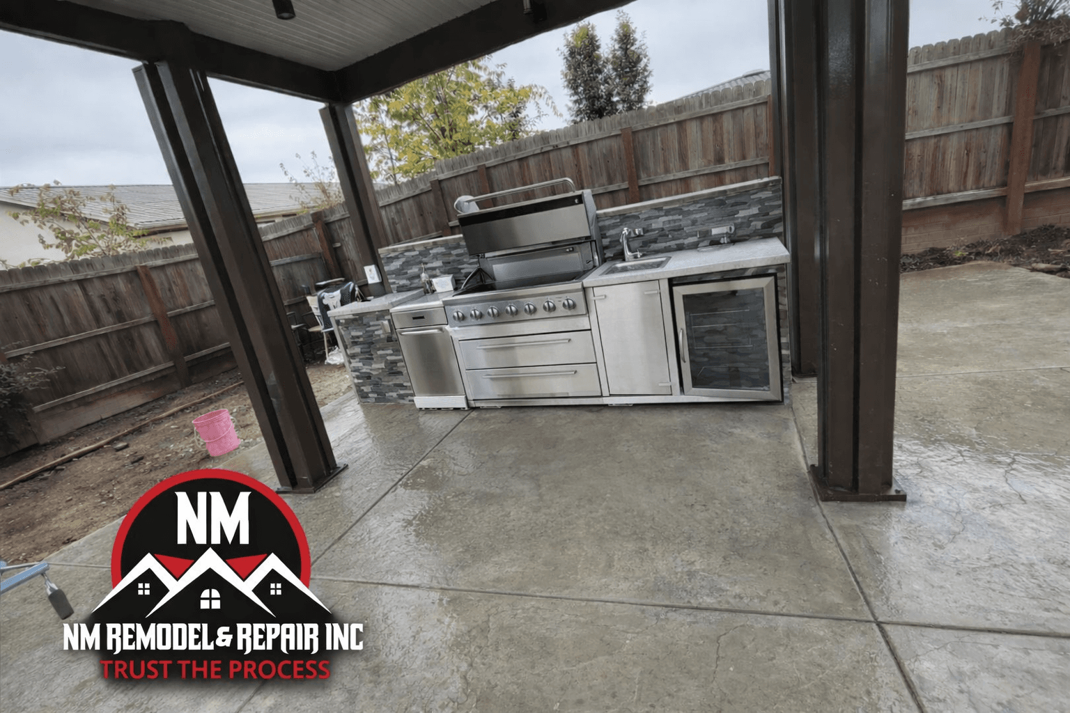 Modern stainless steel outdoor kitchen with grill and sink under a covered patio structure.