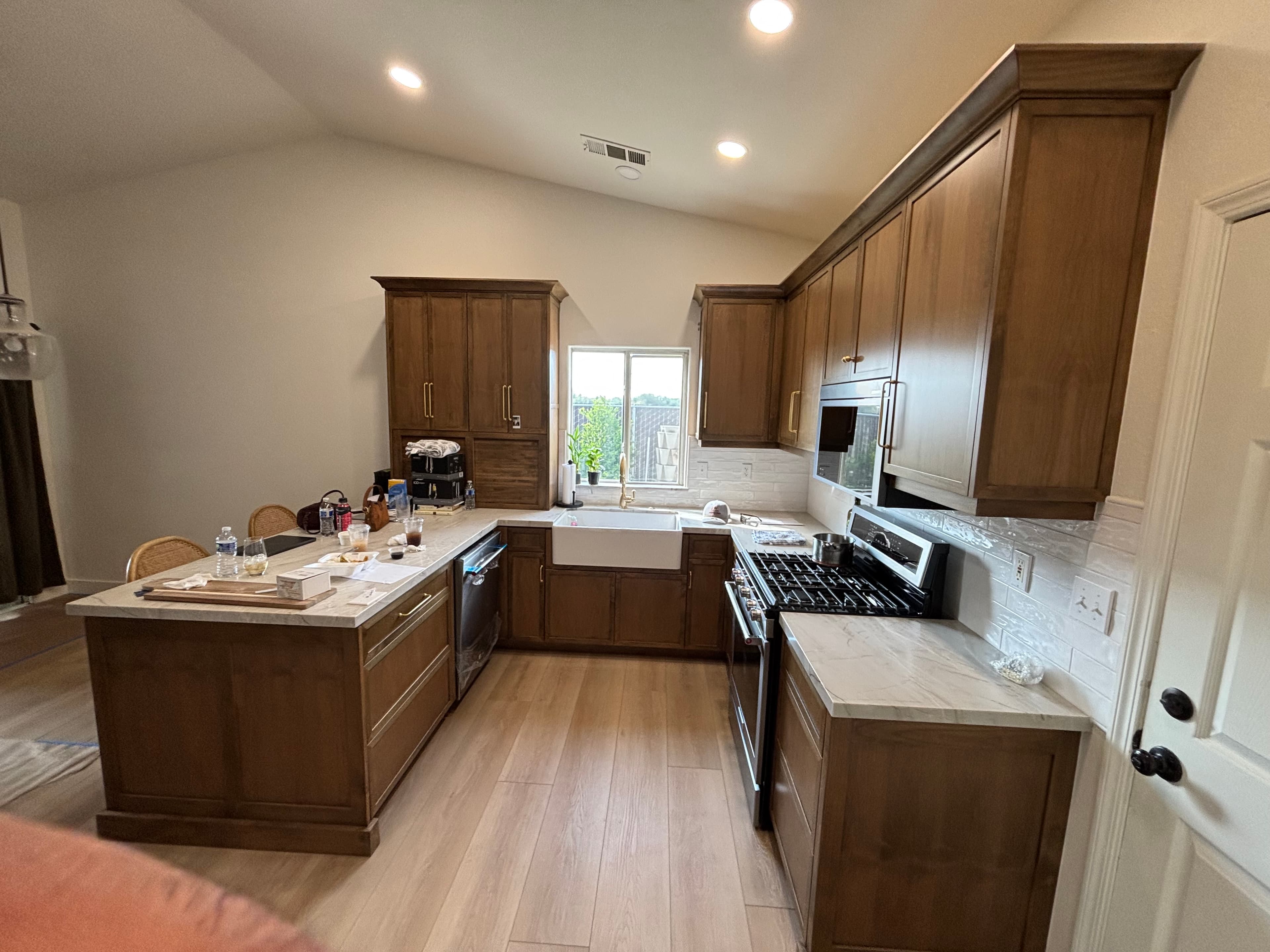 Modern kitchen with brown cabinets, marble countertops, a large island, and light wood flooring.