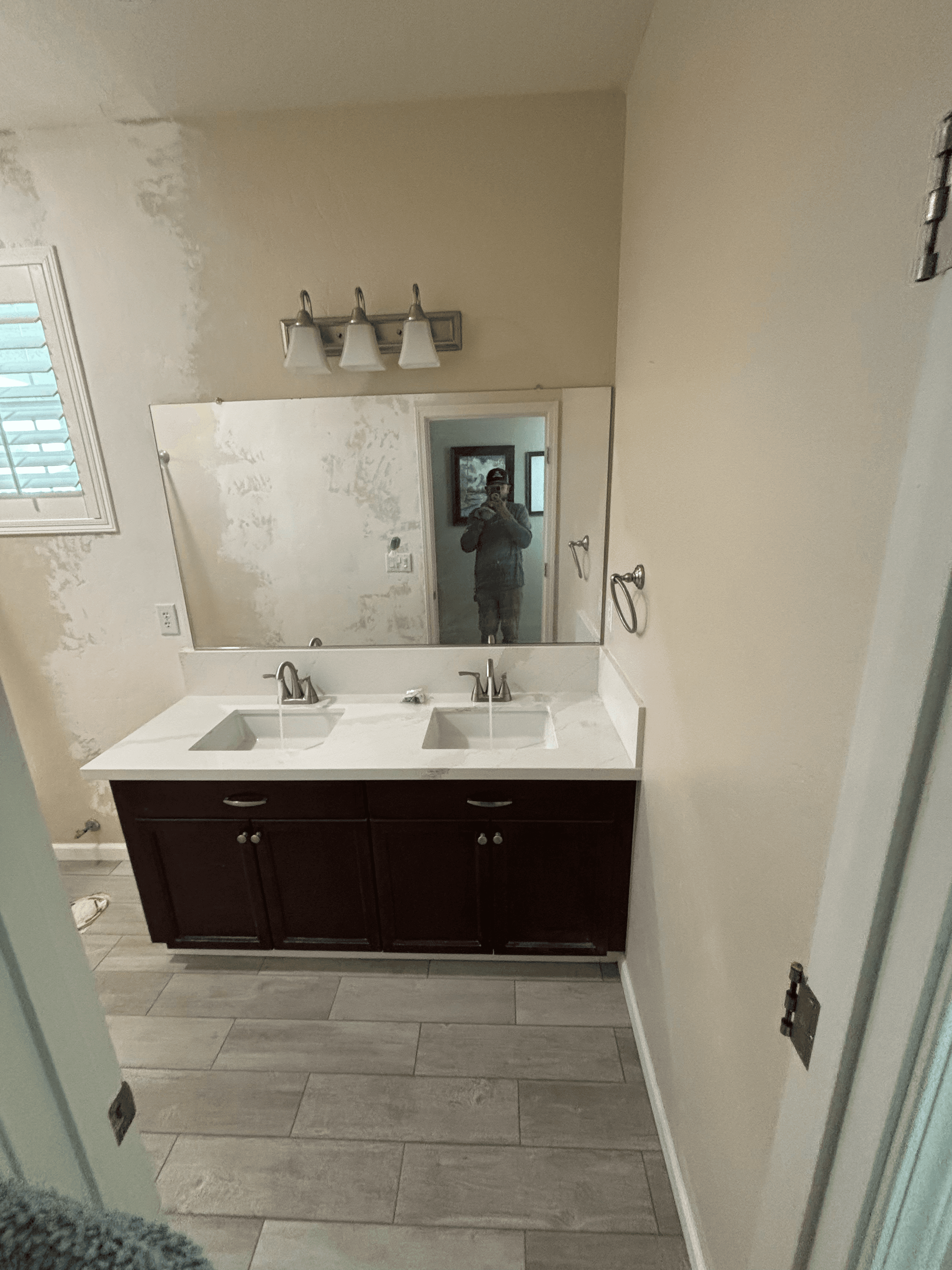 Bathroom double vanity with dark cabinets and white countertop against unfinished, plastered walls.