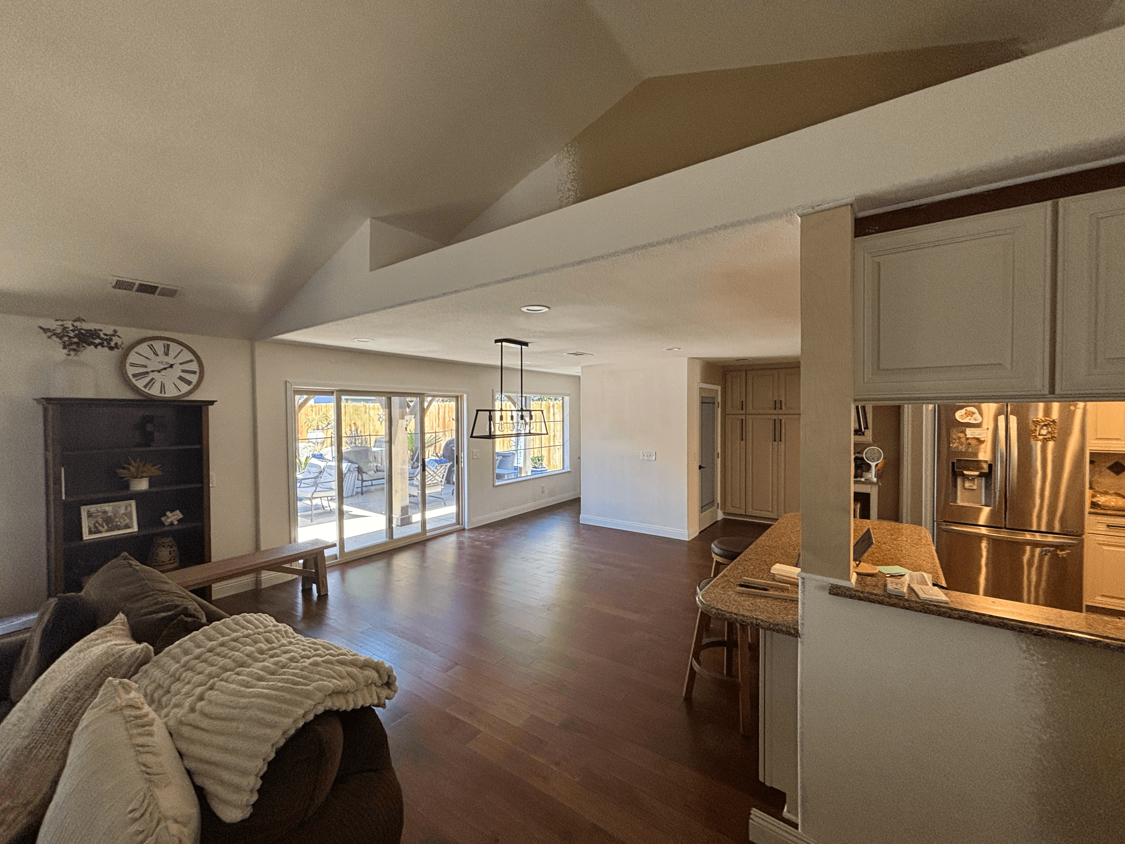 Open living space with dark wood floors, vaulted ceilings, kitchen counter, and sliding glass doors.