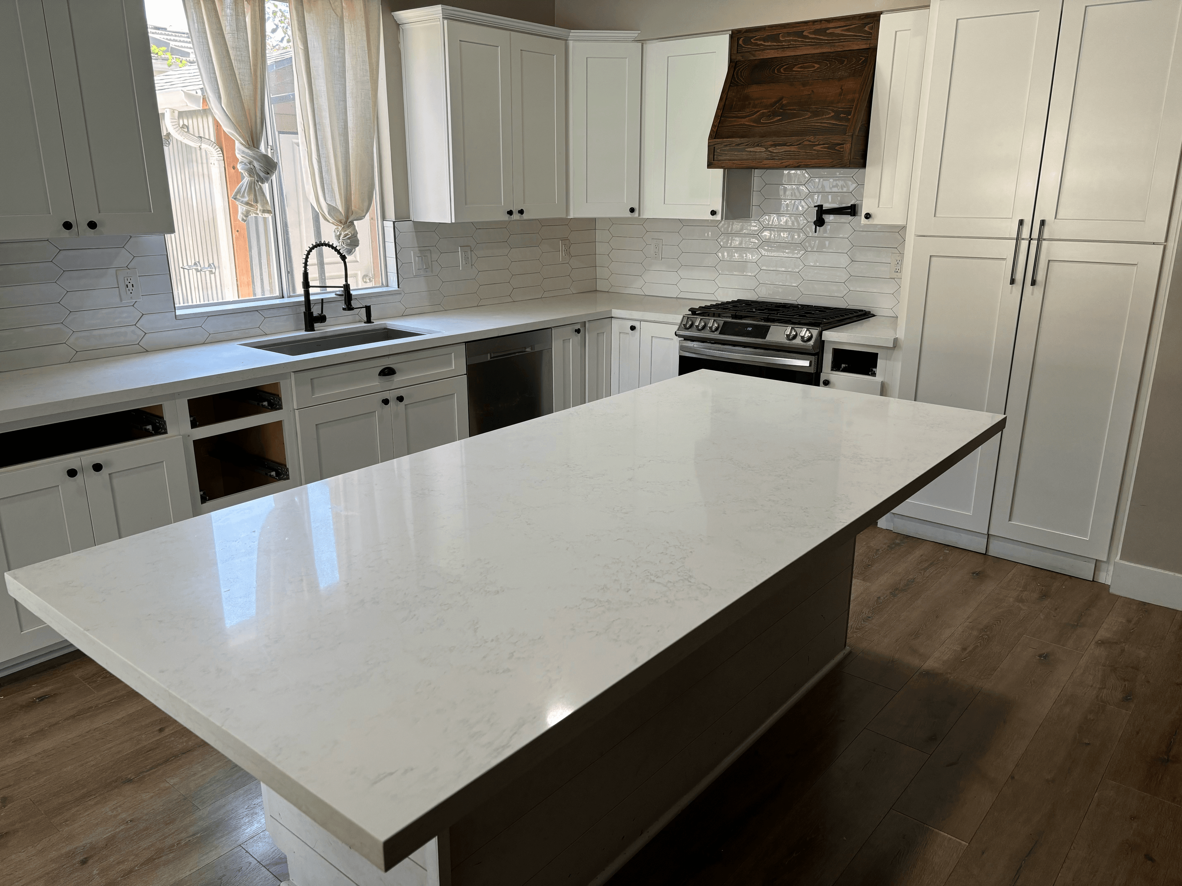 Modern white kitchen featuring a large quartz island and a dark wood range hood.