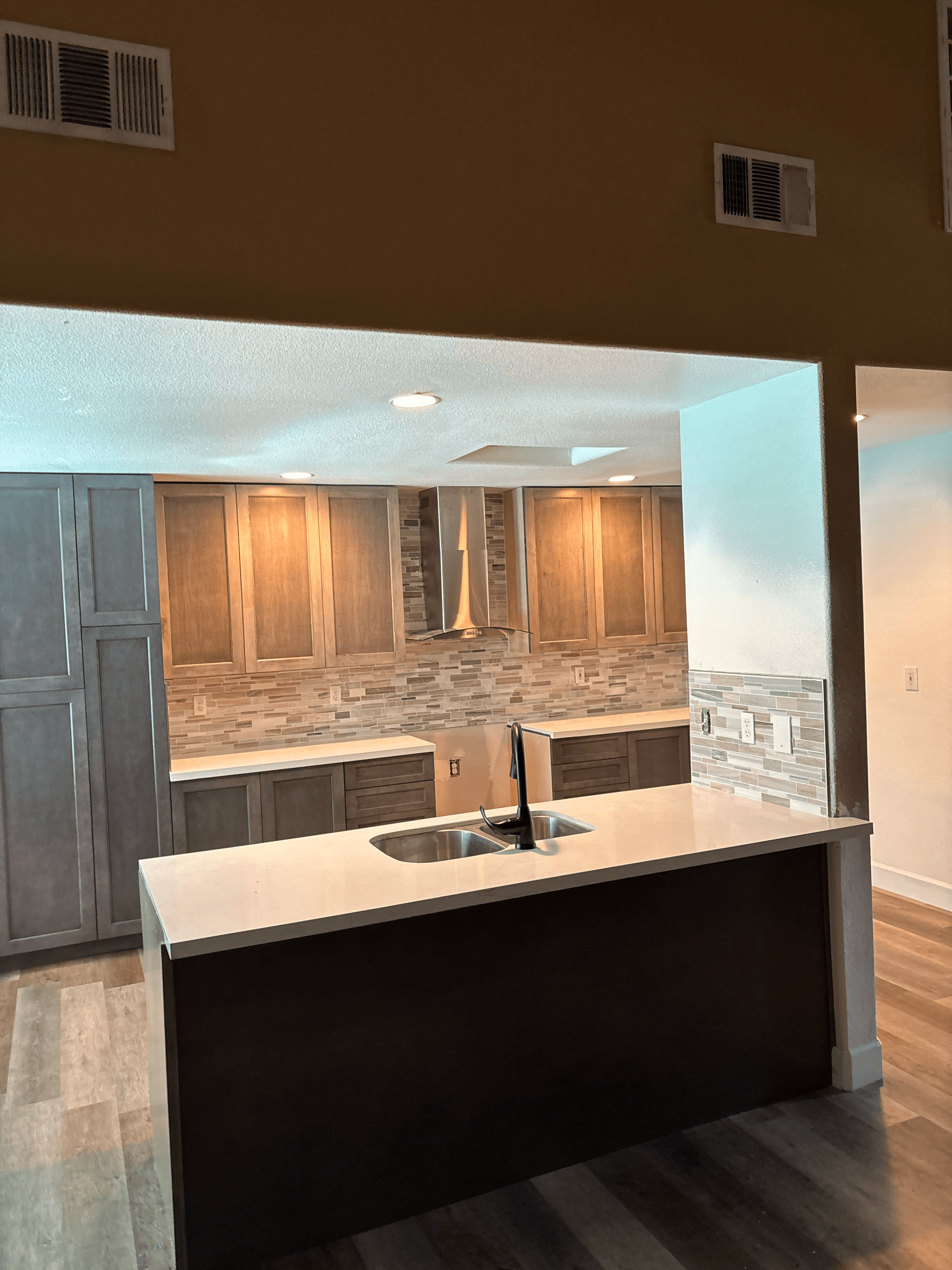 Modern kitchen with dark island, white countertop, wood cabinets, and stainless steel range hood.