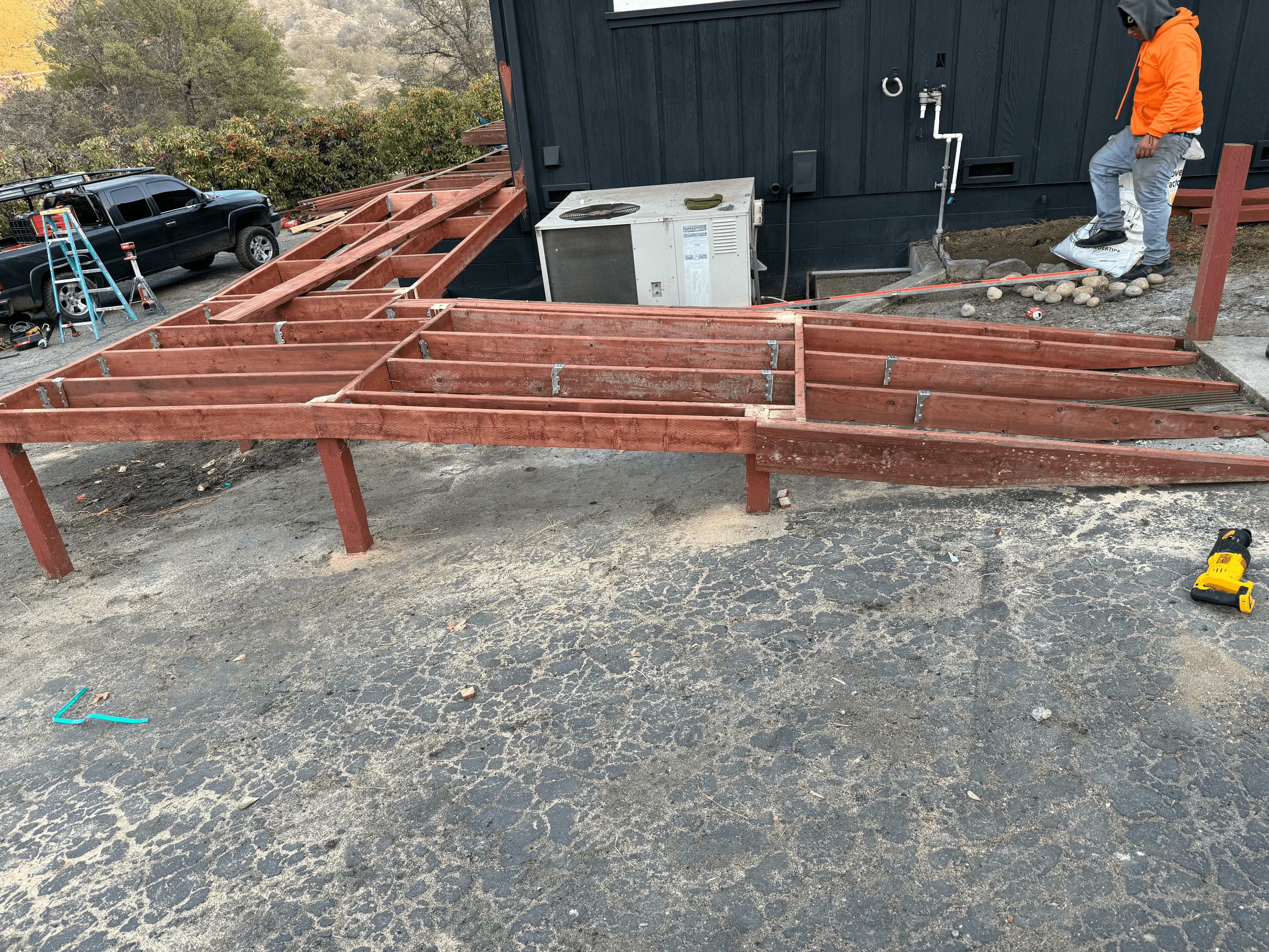 Reddish-brown wooden deck frame under construction against a black house with a worker nearby.